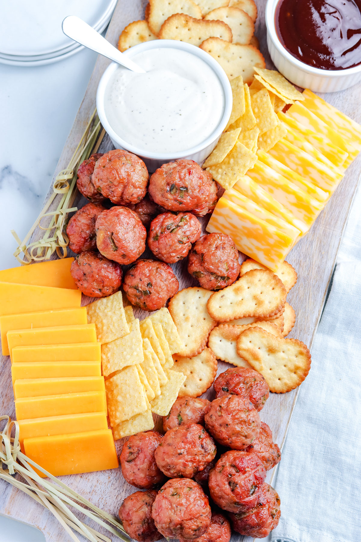 A platter of smoked meatballs along with BBQ sauce, cheese, and crackers,