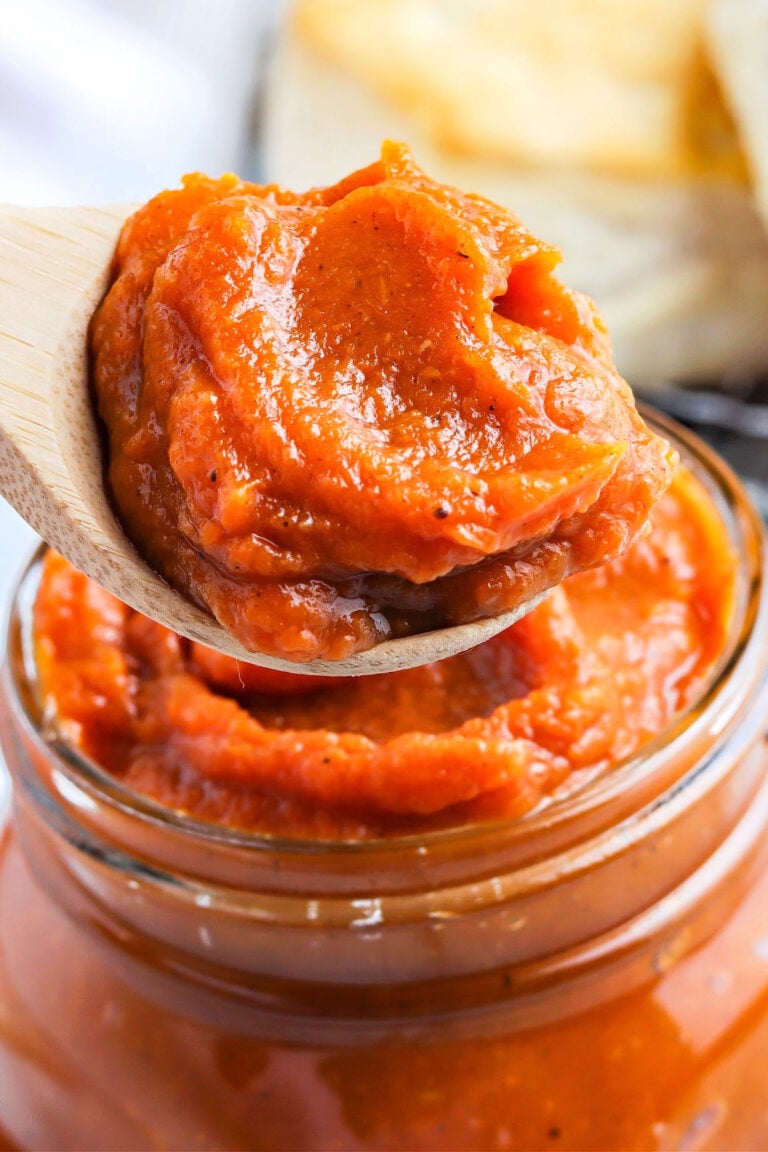 lose-up of a wooden spoon lifting thick, glossy spiced pumpkin butter from a jar.