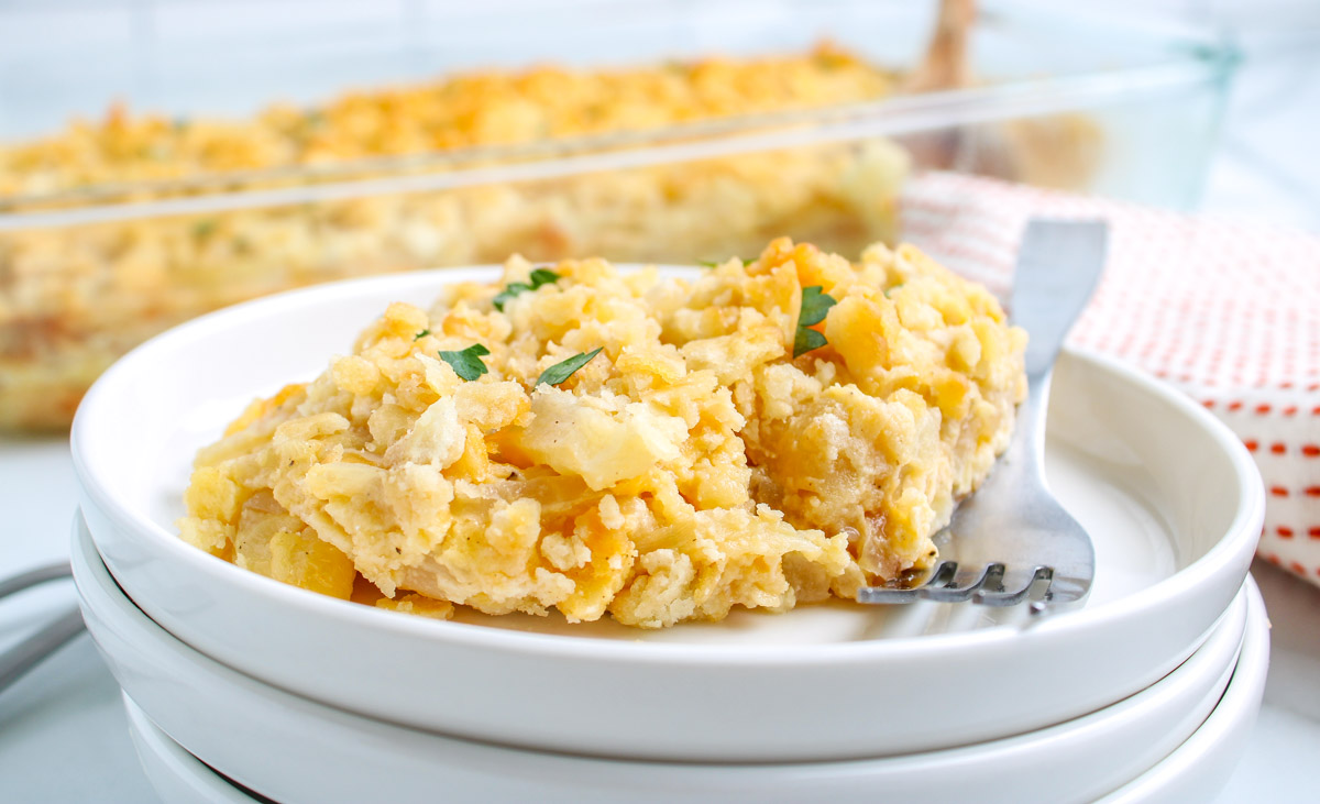 A serving of cheesy sweet onion casserole on a white plate, topped with buttery cracker crumbs and garnished with parsley.