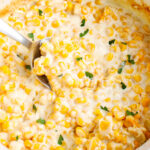 Close-up of creamy crockpot creamed corn with melted cream cheese and butter, sprinkled with fresh parsley and scooped with a serving spoon.