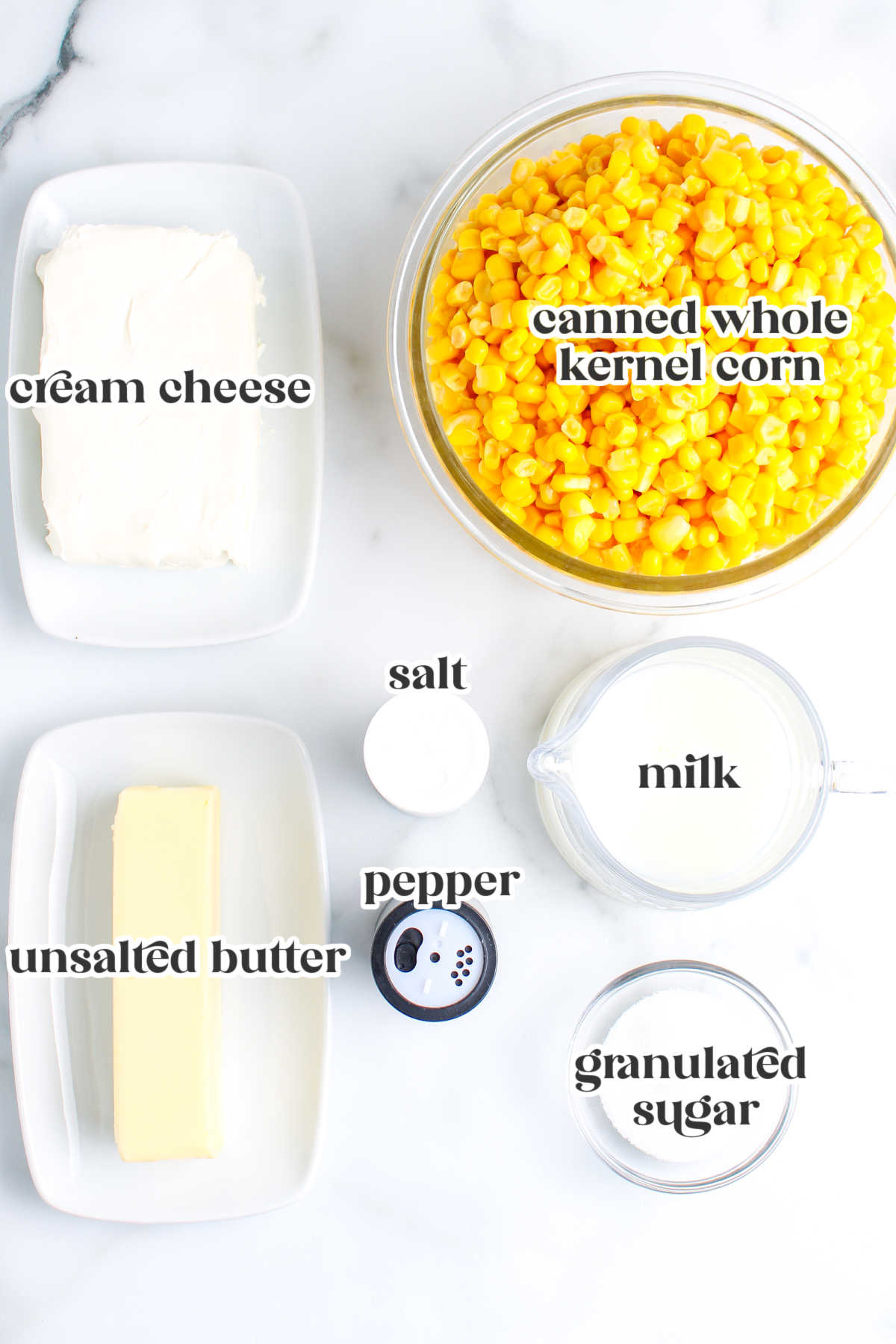 Overhead view of labeled ingredients for crockpot creamed corn including cream cheese, canned corn, butter, milk, sugar, salt, and pepper.