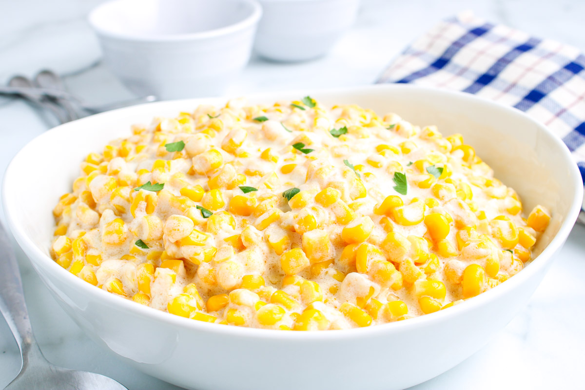 Large white serving bowl filled with creamy corn and garnished with parsley, ready to serve as a side dish.