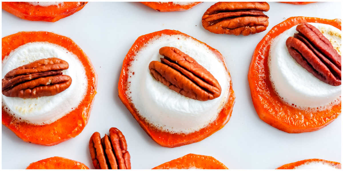 Sweet potato bites topped with gooey toasted marshmallows and crunchy pecan halves arranged on a white background.