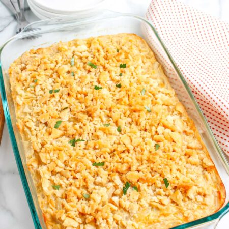 Baked cheesy onion casserole in a glass 13x9 dish with crisp buttery cracker topping and fresh parsley garnish.