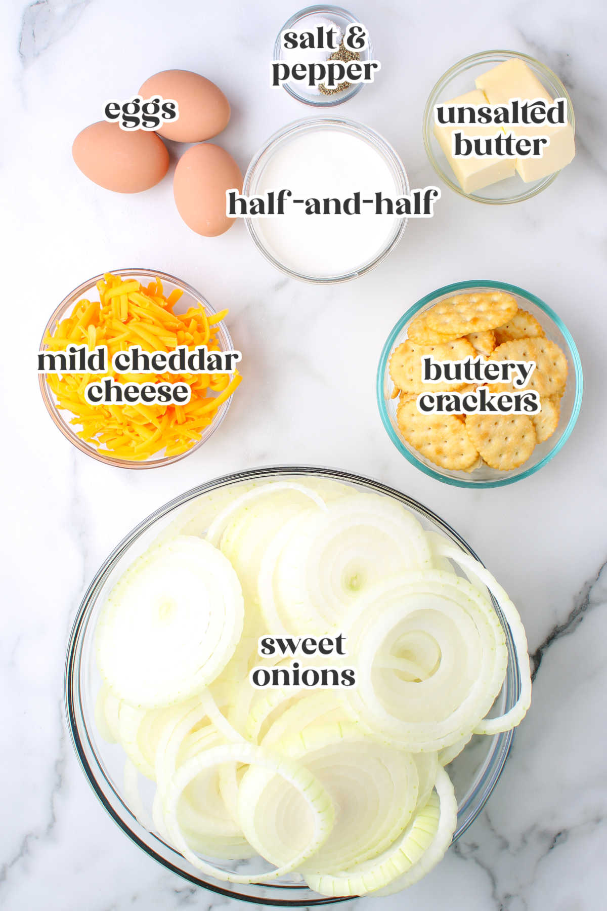 Overhead view of onion casserole ingredients including sliced sweet onions, eggs, cheese, crackers, butter, half-and-half, salt, and pepper.