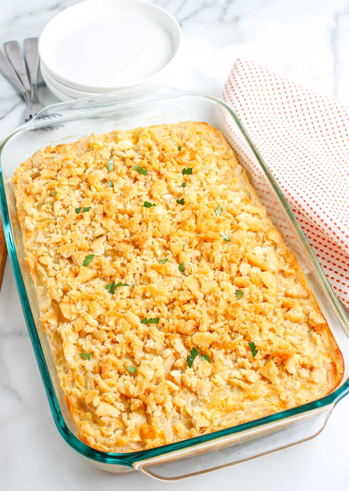 Baked cheesy onion casserole in a glass 13x9 dish with crisp buttery cracker topping and fresh parsley garnish.