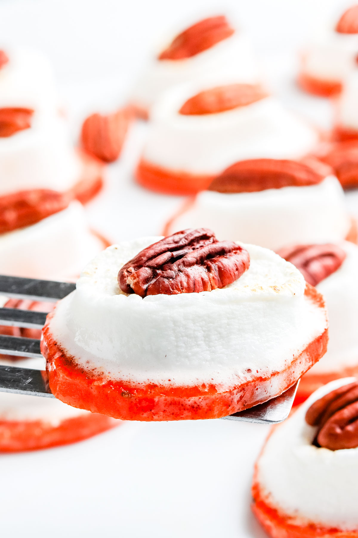A close up of a sweet potato bite topped with melted marshmallow and pecan half being served on a spatula.