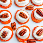 Overhead shot of sweet potato bites topped with toasted marshmallows and pecans arranged in neat rows on a white background.