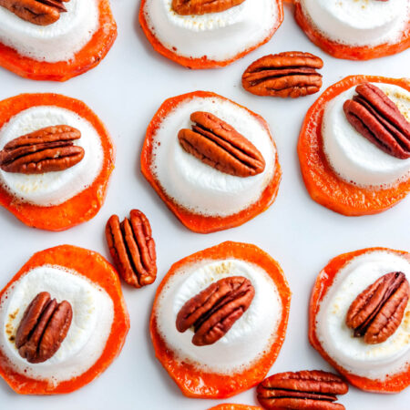 Overhead shot of sweet potato bites topped with toasted marshmallows and pecans arranged in neat rows on a white background.