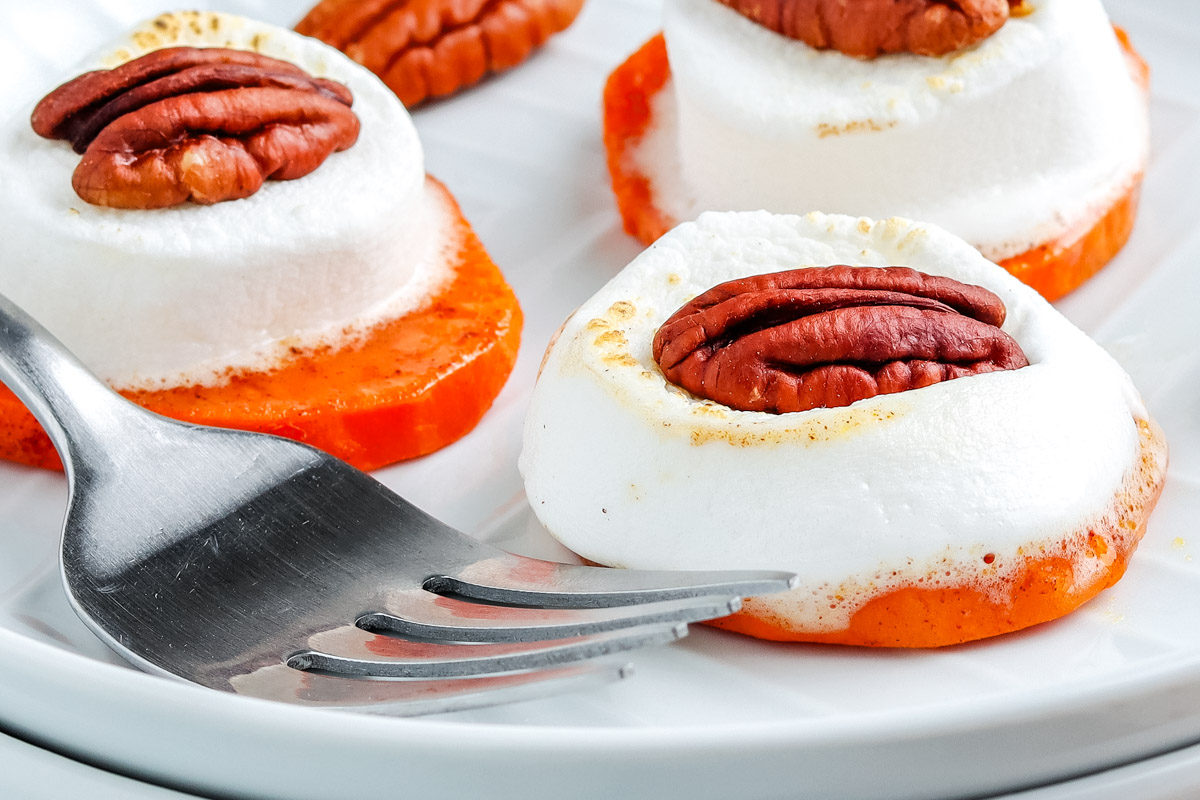 Toasted sweet potato bites with melted marshmallows and pecans on a white plate beside a fork.