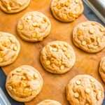 Freshly baked butterscotch cookies on a lined baking sheet with golden tops and visible butterscotch chips.