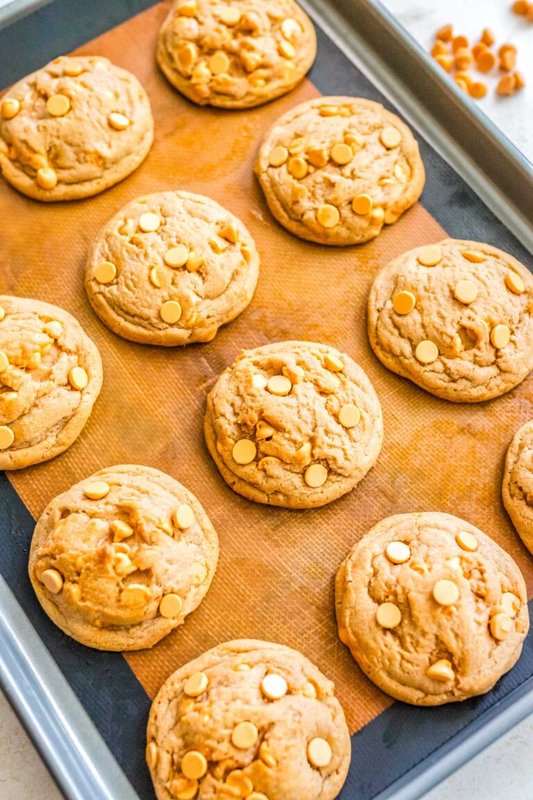 Freshly baked butterscotch cookies on a lined baking sheet with golden tops and visible butterscotch chips.