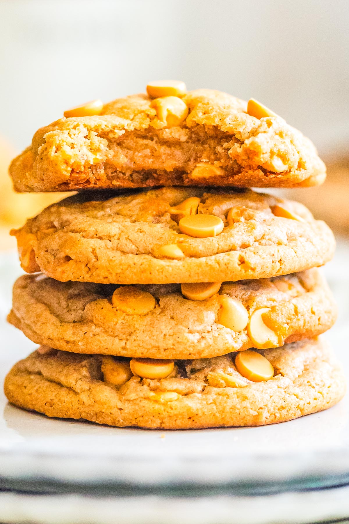 Tall stack of soft chewy butterscotch cookies with visible butterscotch chips and a bite taken from the top cookie showing the gooey center.
