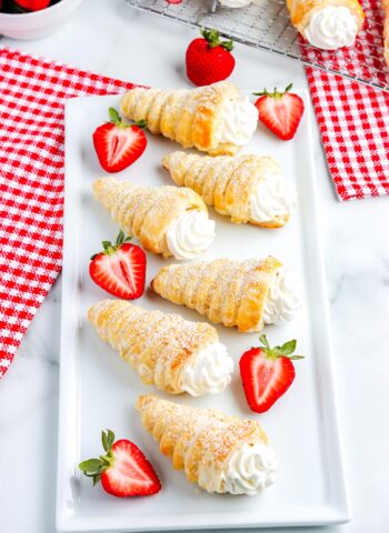 Italian-style puff pastry cream horns topped with powdered sugar and served with strawberries on a white plate, perfect for dessert or brunch.
