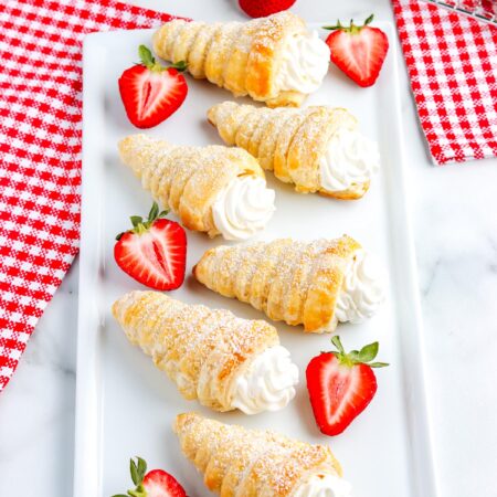 Italian-style puff pastry cream horns topped with powdered sugar and served with strawberries on a white plate, perfect for dessert or brunch.