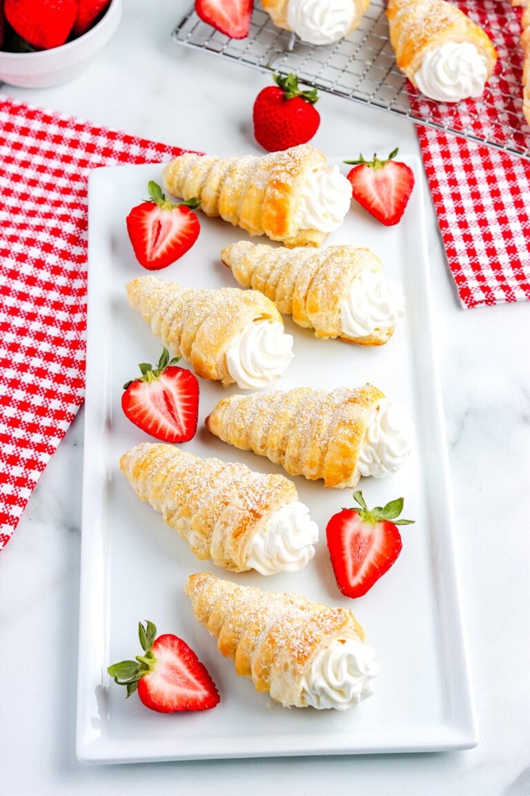 Italian-style puff pastry cream horns topped with powdered sugar and served with strawberries on a white plate, perfect for dessert or brunch.