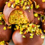 Close-up of a bitten Dubai Chocolate Truffle revealing the creamy green pistachio and crunchy kataifi filling, topped with chopped pistachios.