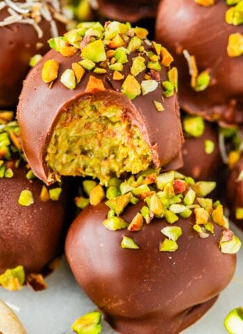 Close-up of a bitten Dubai Chocolate Truffle revealing the creamy green pistachio and crunchy kataifi filling, topped with chopped pistachios.