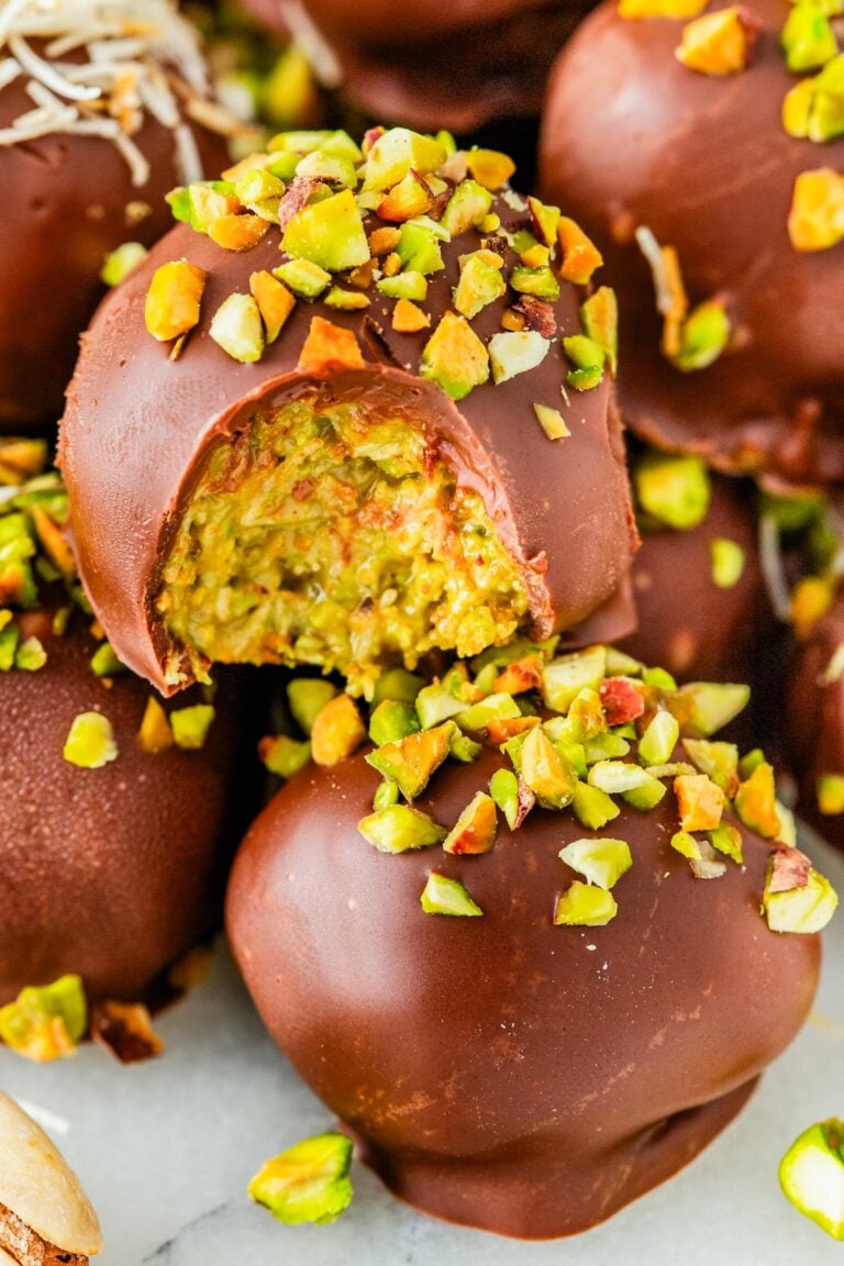 Close-up of a bitten Dubai Chocolate Truffle revealing the creamy green pistachio and crunchy kataifi filling, topped with chopped pistachios.