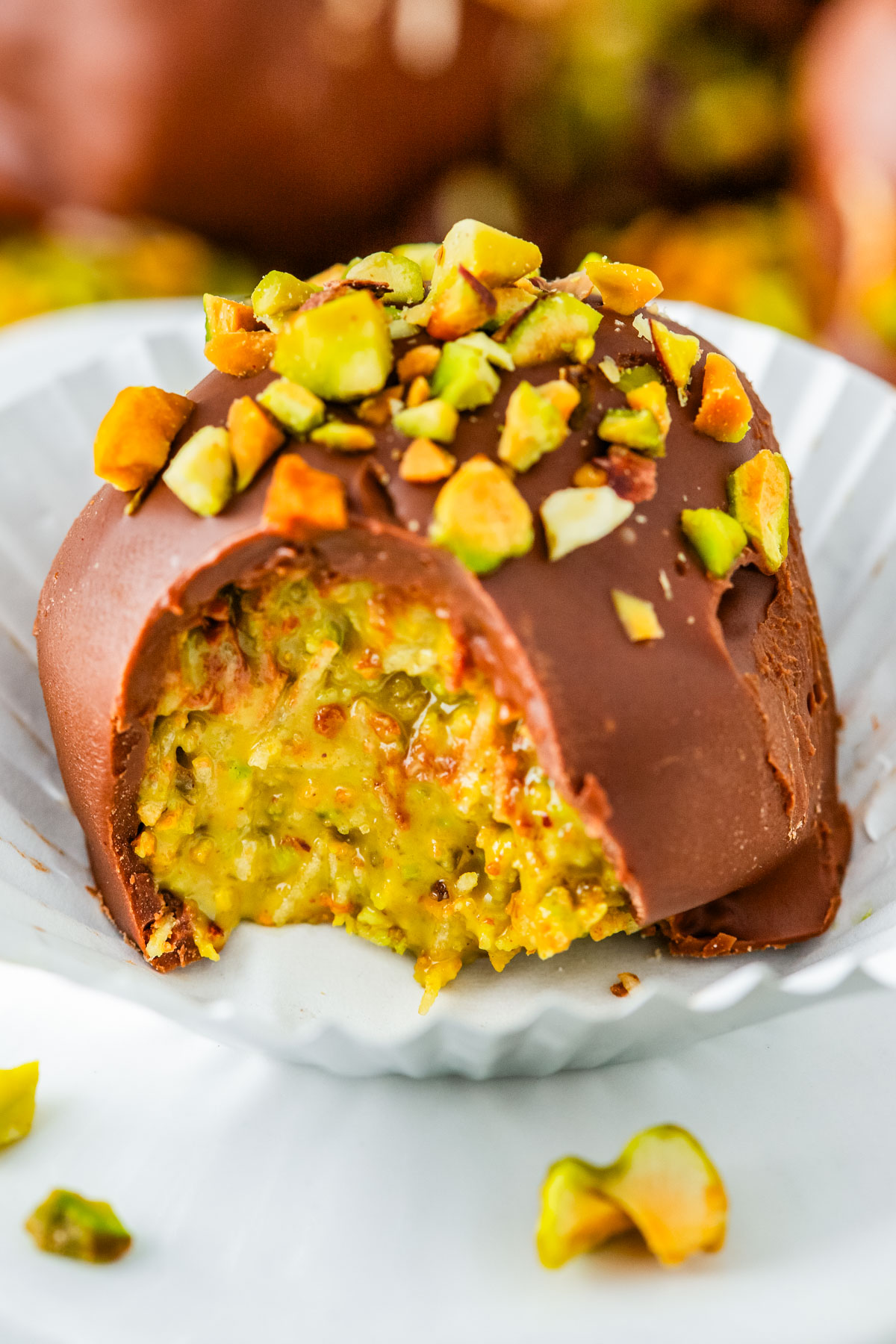 A single Dubai Chocolate Truffle in a white paper liner with a bite taken out, showing the vibrant green pistachio and crunchy kataifi center.