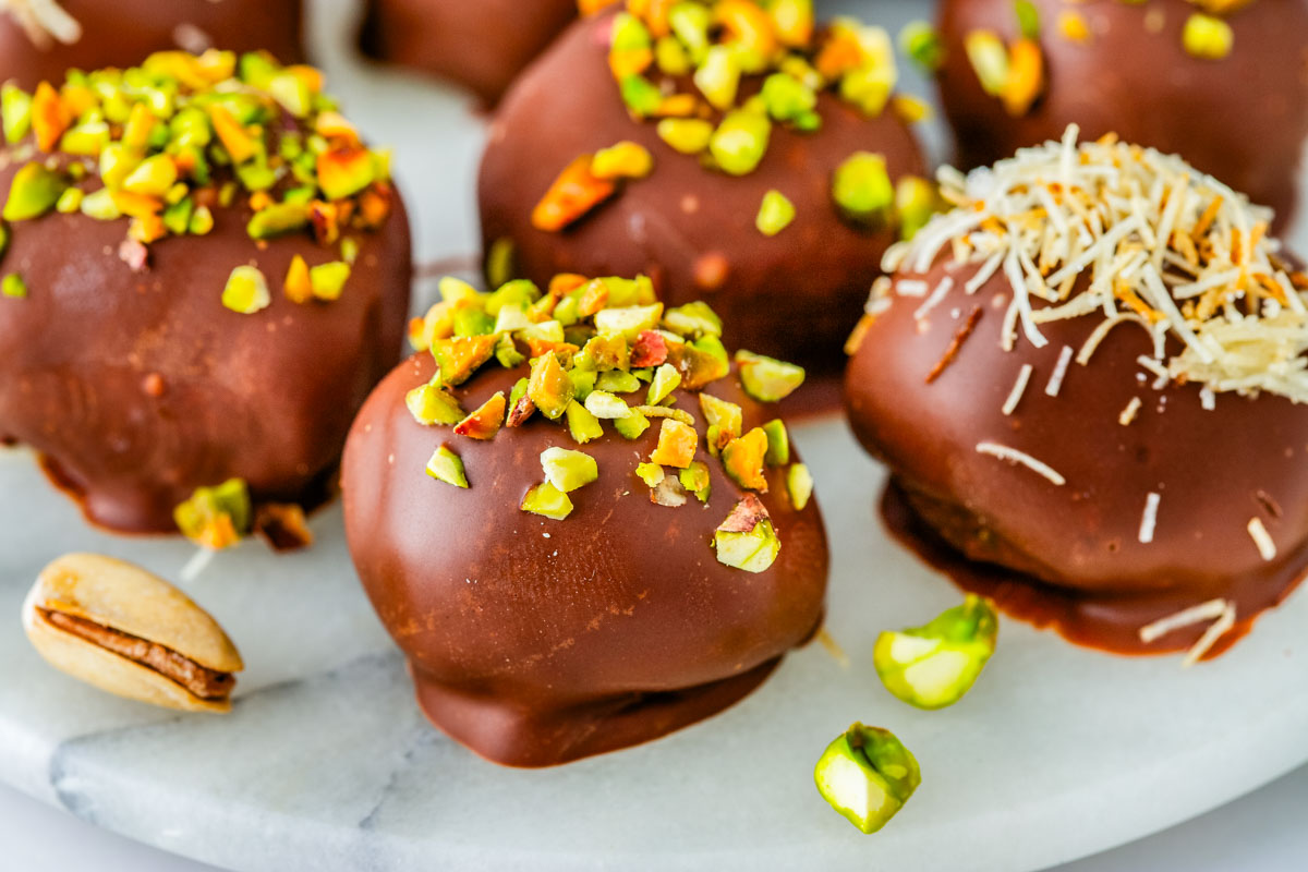 A platter of finished Dubai Chocolate Truffles garnished with chopped pistachios and shredded coconut, sitting on a marble serving board.