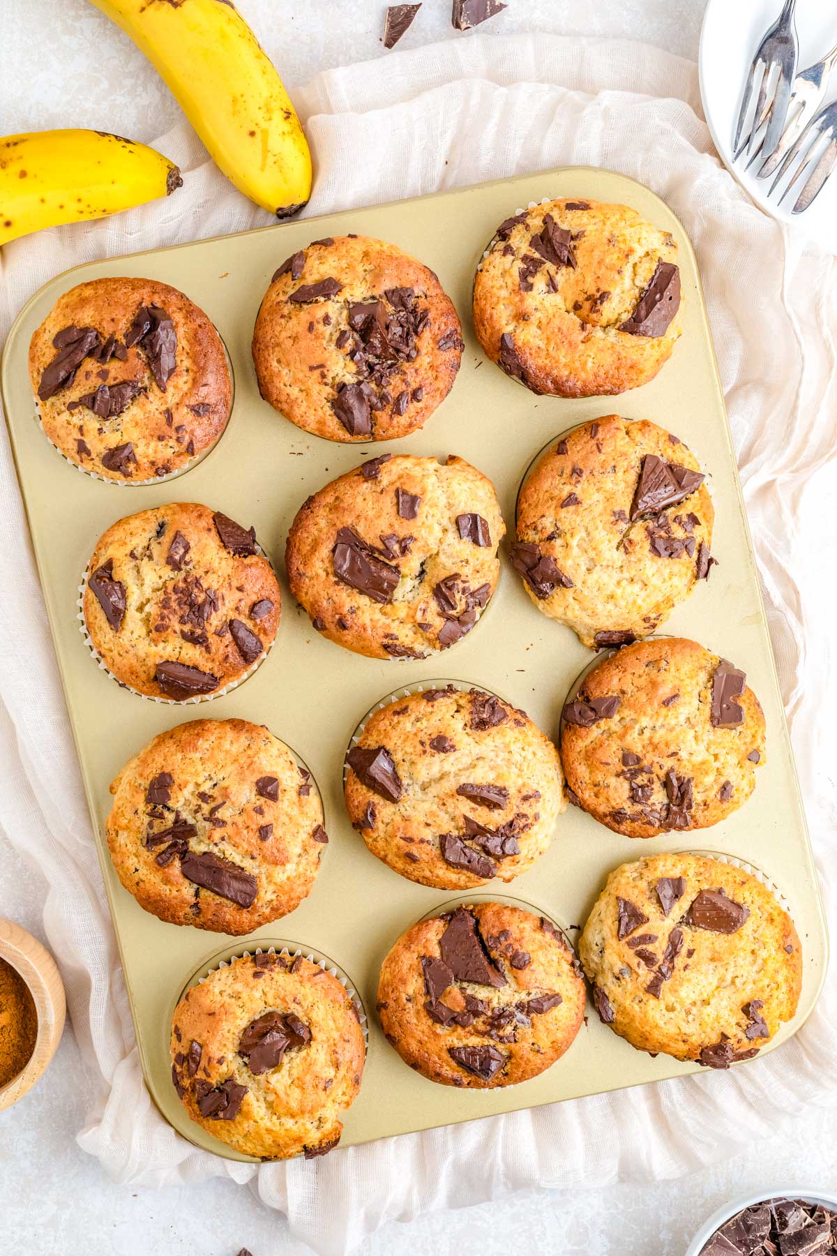 Overhead view of freshly baked chocolate chunk banana muffins in a muffin pan with golden tops and large chocolate pieces.