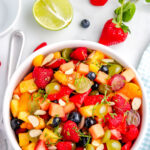 Overhead view of fruit salad with lime zest and honey dressing, filled with mixed berries, grapes, pineapple, and cantaloupe.