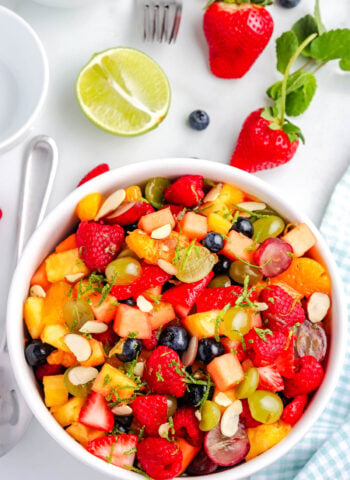 Overhead view of fruit salad with lime zest and honey dressing, filled with mixed berries, grapes, pineapple, and cantaloupe.