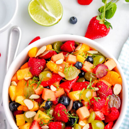 Overhead view of fruit salad with lime zest and honey dressing, filled with mixed berries, grapes, pineapple, and cantaloupe.