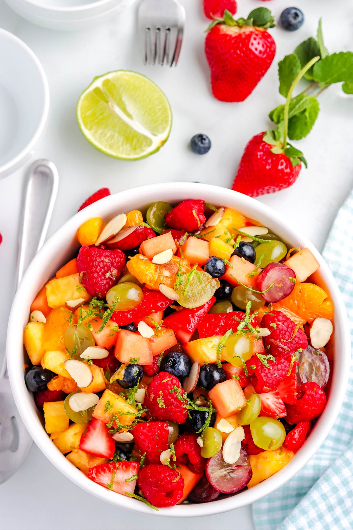 Overhead view of fruit salad with lime zest and honey dressing, filled with mixed berries, grapes, pineapple, and cantaloupe.