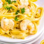 Plate of creamy garlic Parmesan shrimp pasta garnished with parsley and lemon slices on a light background.