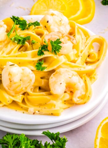 Plate of creamy garlic Parmesan shrimp pasta garnished with parsley and lemon slices on a light background.