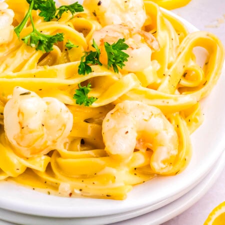 Plate of creamy garlic Parmesan shrimp pasta garnished with parsley and lemon slices on a light background.