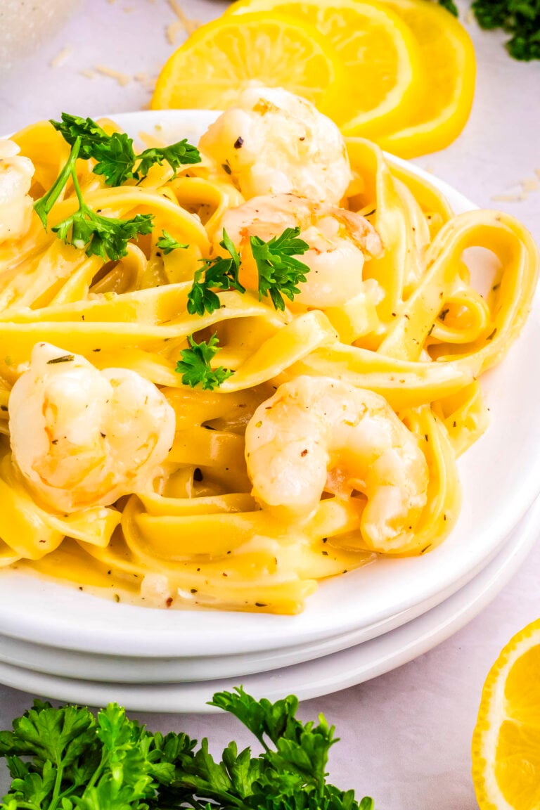 Plate of creamy garlic Parmesan shrimp pasta garnished with parsley and lemon slices on a light background.