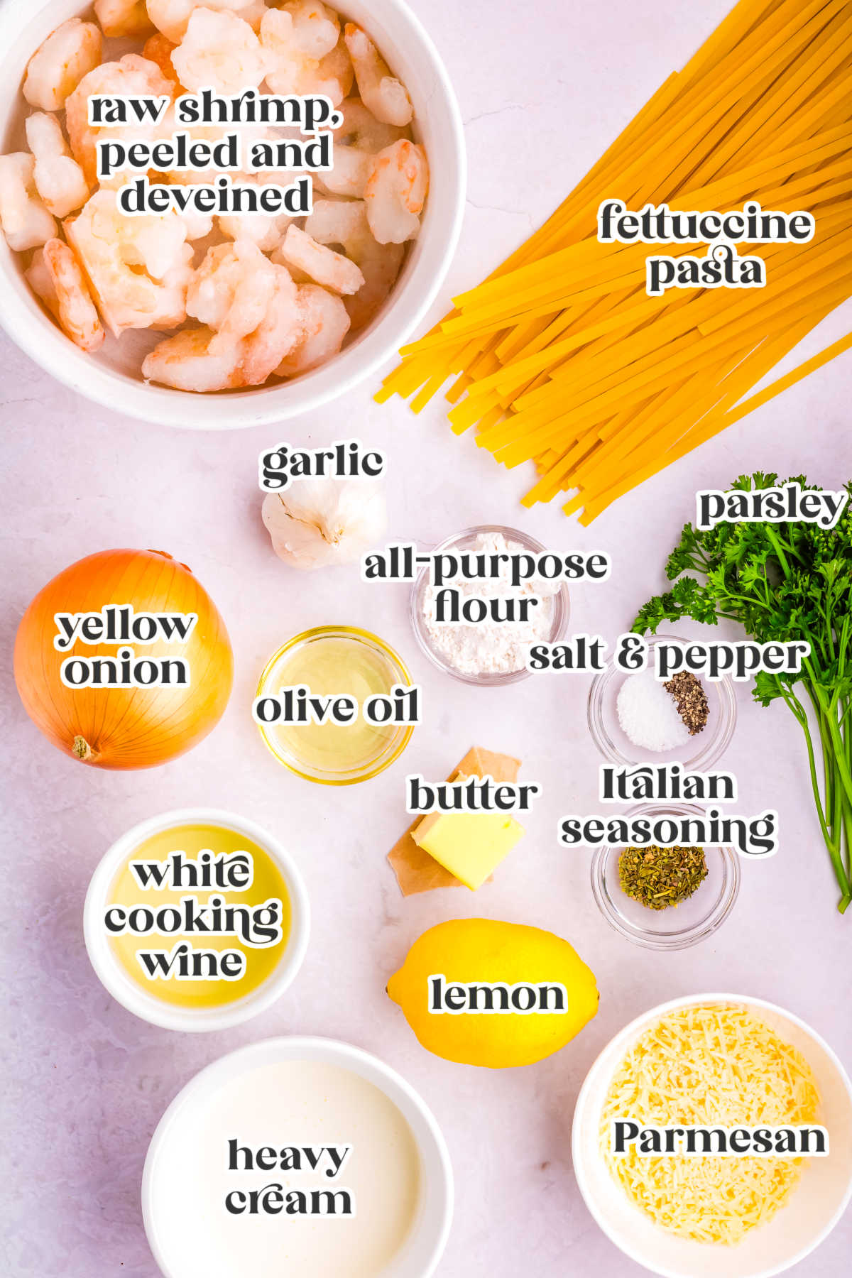 Overhead view of ingredients for garlic Parmesan shrimp pasta including shrimp, fettuccine, Parmesan cheese, lemon, garlic, onion, cream, parsley, and seasonings.