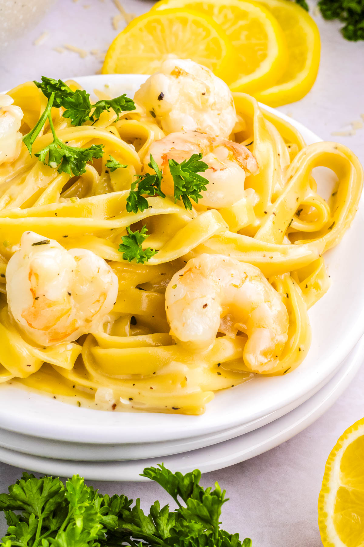 Plate of creamy garlic Parmesan shrimp pasta garnished with parsley and lemon slices on a light background.