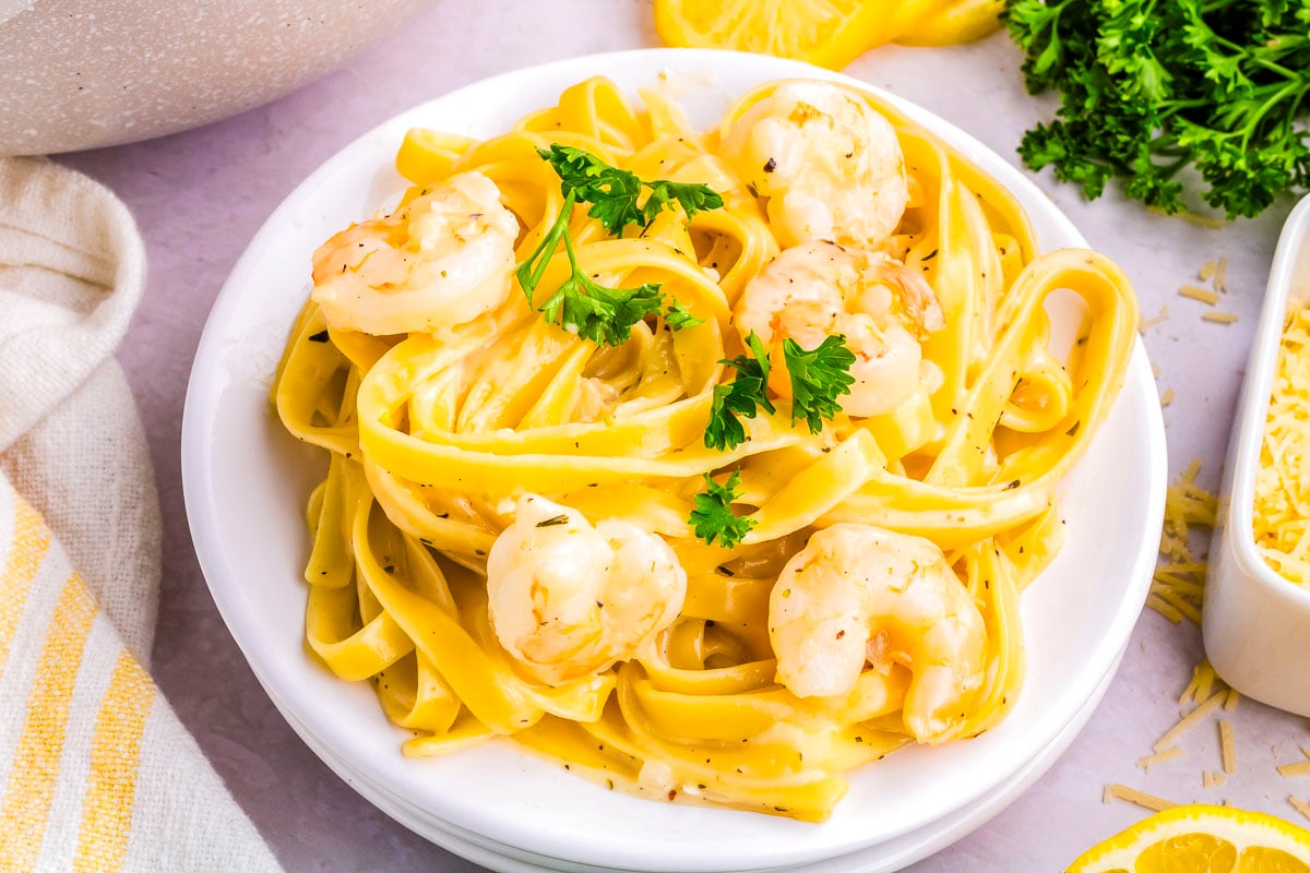 Bowl of creamy garlic Parmesan shrimp pasta with fettuccine noodles, parsley garnish, and lemon slices beside the plate.