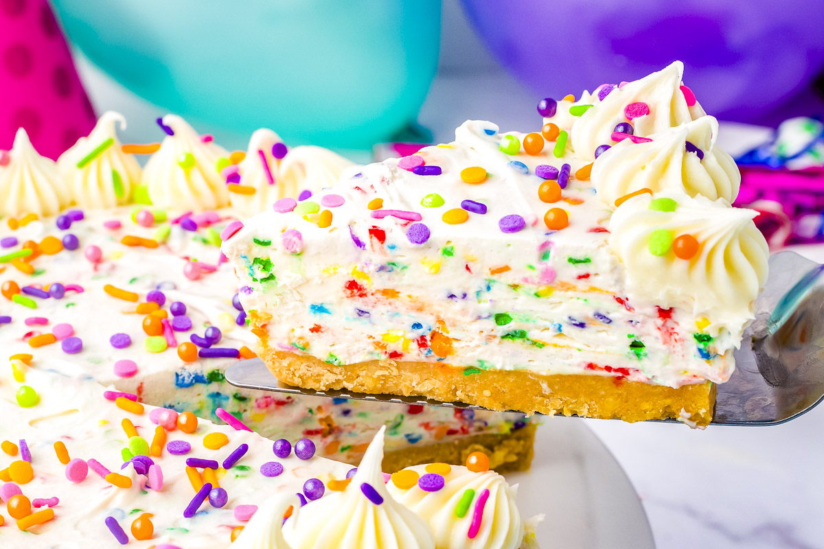 Slice of no bake funfetti cheesecake lifted from the pan with rainbow sprinkles, piped vanilla icing, and golden cookie crust.
