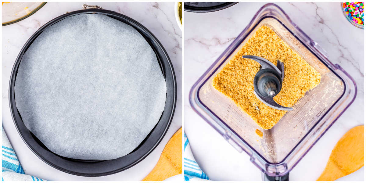 Parchment lined springform pan beside a blender filled with crushed golden cookie crumbs for cheesecake crust preparation.