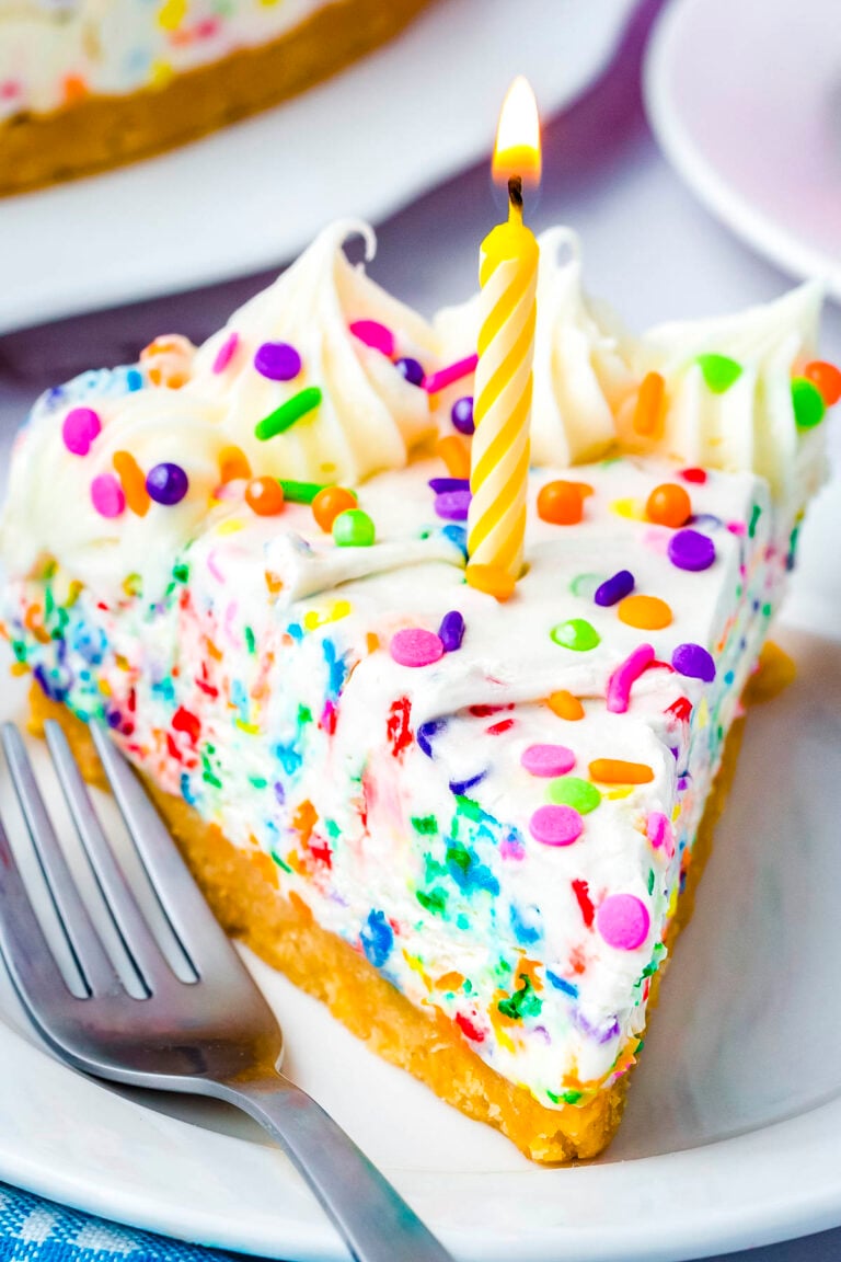 Slice of no-bake funfetti cheesecake with rainbow sprinkles and a birthday candle on a white dessert plate.